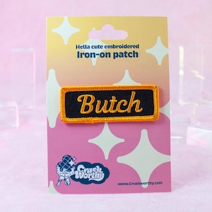 May include: A yellow and black iron-on patch with the word "Butch" embroidered in yellow on a black background. The patch is on a pink and white background with the text "Hella cute embroidered iron-on patch" and "Crush Worthy" logo.