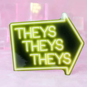 May include: A neon green arrow-shaped pin with the word "THEYS" repeated three times in white. The pin has a black background and a neon-style border. The background is a soft pink.