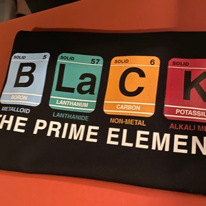 May include: Black t-shirt with a graphic of the periodic table elements spelling out the word "BLACK". The elements are Boron, Lanthanum, Carbon, and Potassium. The text "THE PRIME ELEMENT" is printed below the graphic.