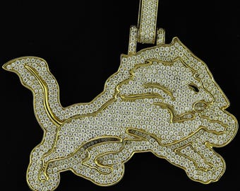 May include: A gold-toned pendant in the shape of a lion, encrusted with numerous small, sparkling stones. The lion is depicted in a running pose, with a detailed mane and tail. The pendant has a loop for a chain.