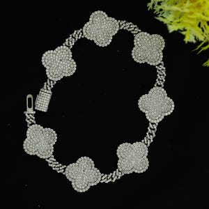 May include: A silver chain necklace with a clover design. Each clover is encrusted with clear cubic zirconia stones.