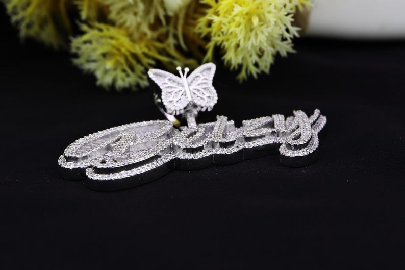 May include: A silver pendant with a butterfly charm and the word "Betsy" spelled out in sparkling rhinestones.