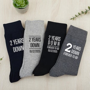 May include: Four pairs of socks with the text "2 Years Down" and a date. Two pairs are black, one is gray, and one is dark gray.