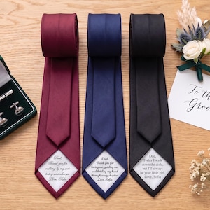 Puede incluir: Tres corbatas en color burdeos, azul marino y negro, cada una con un parche de tela blanca cosido en la punta trasera con mensajes personalizados en negro. La corbata burdeos dice, Dad, Thank you for walking by my side today and always. Love, Sofia.