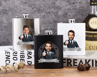 May include: Three stainless steel, black, and white flasks with personalized images and names. Each flask features a silver cap and a banner with a name. The flasks are on a wooden surface with books and a bottle of liquor in the background.