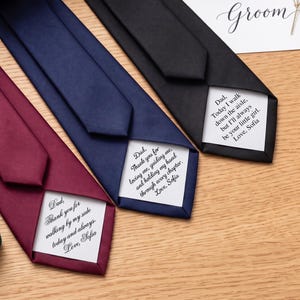 May include: Three neckties in burgundy, navy blue, and black, each featuring a white fabric patch sewn onto the underside. The patches contain printed messages addressed to a father from Sofia, expressing gratitude and love for a wedding day.