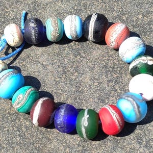 May include: A strand of colorful glass beads with white and silver accents. The beads are round and have a variety of patterns and textures.
