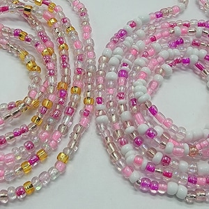 Puede incluir: Un conjunto de cadenas de cintura de cuentas en rosa, blanco y dorado. Las cadenas están hechas de cuentas pequeñas e iridiscentes y están dispuestas en un diseño en capas.