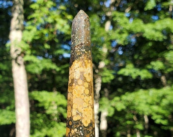 May include: A yellow, brown, and green bumblebee jasper crystal point. The crystal is polished and has a pointed tip. The crystal is about 4 inches long.
