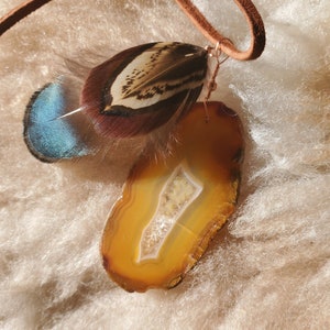 May include: A brown leather cord with a brown and blue feather and a yellow agate slice pendant.