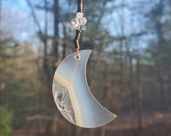 May include: A silver crescent moon charm with a white agate stone, hanging from a black metal key ring with a clear crystal bead.