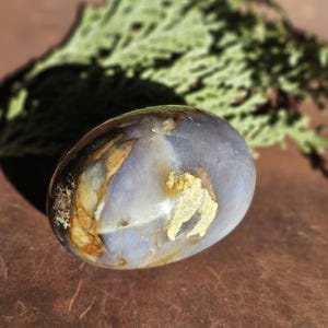 May include: A smooth, polished, light purple and brown agate stone with a unique, swirling pattern. The stone is oval-shaped and has a glossy finish.