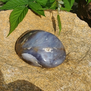 May include: A smooth, polished, gray and brown agate stone with white and brown markings. The stone is oval shaped and has a glossy finish.