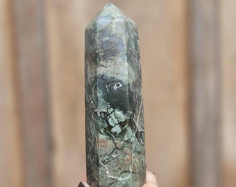 May include: A green and gray crystal point with a pointed tip. The crystal has a natural, rough texture and is a popular choice for crystal healing.