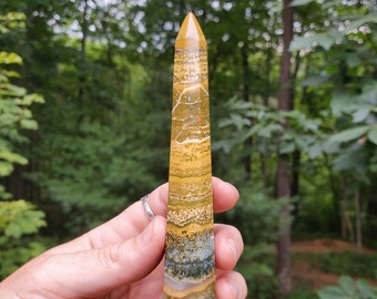 May include: A yellow, green, and white banded crystal point, also known as a crystal wand, is held in a hand. The crystal is about 6 inches long and has a pointed tip.