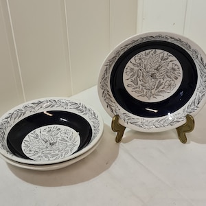 May include: Three white ceramic bowls with a black and white floral design. The bowls have a dark blue rim and a dark blue centre.