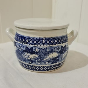 May include: A white ceramic jar with a blue and white floral pattern. The jar has a lid and two handles.