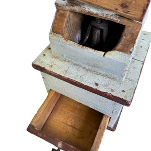 May include: Antique wooden coffee grinder with a drawer and a metal grinding mechanism. The grinder is painted white with red accents and has a wooden handle.