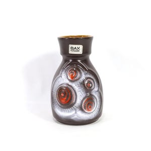 Puede incluir: Un jarrón de cerámica marrón con un diseño de espiral blanco y rojo. El jarrón tiene una etiqueta que dice "BAY. KERAMIK."