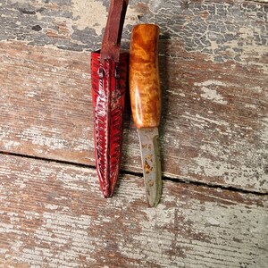 Puede incluir: Un peque&ntilde;o cuchillo con mango de madera y una funda de cuero. El cuchillo tiene una hoja lisa y la funda es roja con un patr&oacute;n decorativo.
