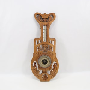 May include: A vintage wooden barometer with a thermometer. The barometer is carved with floral and scroll designs. The thermometer is in a glass tube. The wooden frame is a light brown color.