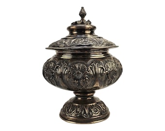 May include: An ornate silver sugar bowl with a lid and a decorative base. The bowl is decorated with intricate floral patterns.