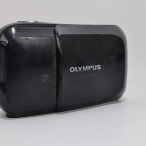 Olympus Mju I 35mm compact film camera in black finish with sliding lens cover. Tested and fully working with film. Flash functions properly. Features Olympus 35mm f3.5 lens and autofocus system. Classic 1990s point and shoot camera with clean lens and functional film compartment. Minor cosmetic wear from age. Vintage compact camera ready for use.
