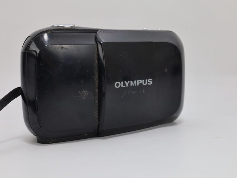 Olympus Mju I 35mm compact film camera in black finish with sliding lens cover. Tested and fully working with film. Flash functions properly. Features Olympus 35mm f3.5 lens and autofocus system. Classic 1990s point and shoot camera with clean lens and functional film compartment. Minor cosmetic wear from age. Vintage compact camera ready for use.
