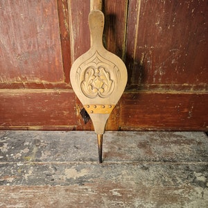 May include: A wooden bellows with a carved floral design and metal accents. The bellows is brown and has a long, pointed nozzle.