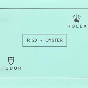 Peut inclure: Une page vert clair d'un catalogue avec les logos Rolex et Tudor. Le texte "R 20 - OYSTER" est centré dans un encadré. Le logo Rolex est une couronne, et le logo Tudor est un bouclier.