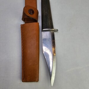 May include: A brown leather sheath with a metal snap closure and a silver knife with a wooden handle.