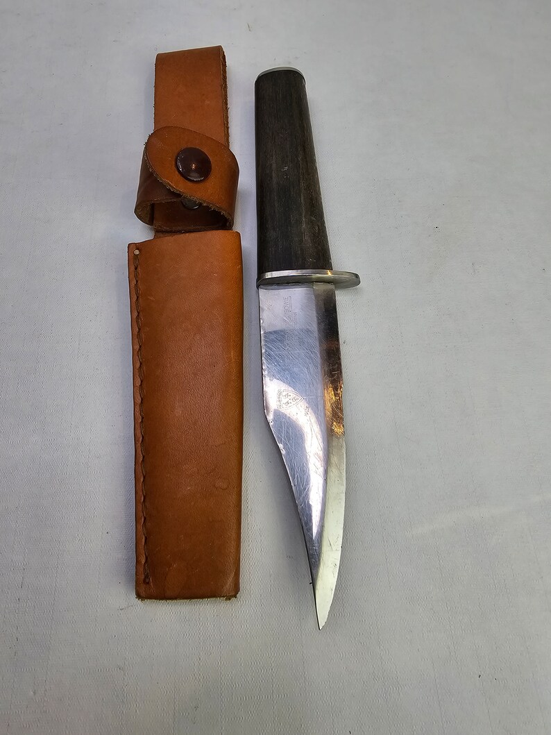 May include: A brown leather sheath with a metal snap closure and a silver knife with a wooden handle.