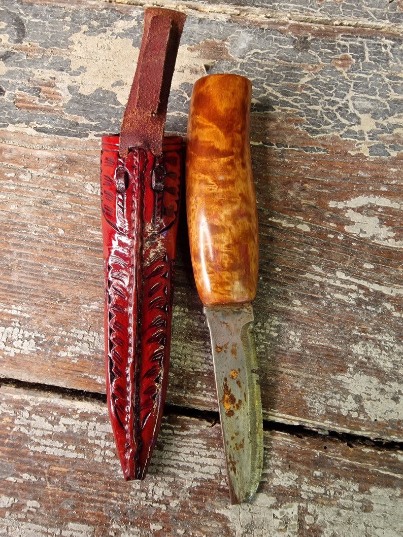 Puede incluir: Una peque&ntilde;a funda de cuchillo de cuero rojo con un cuchillo de mango de madera y una hoja oxidada.