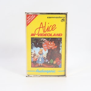 Puede incluir: Un cartucho de juego Commodore 64 vintage para "Alice in Videoland". La etiqueta amarilla presenta el título en una fuente caprichosa, una colorida ilustración de Alicia y el Gato de Cheshire, y el logotipo "Audiogenic".