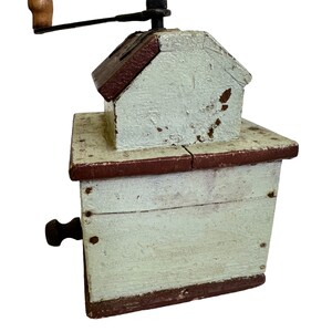 May include: A vintage wooden coffee grinder with a hand crank. The grinder is painted white with brown accents and has a small wooden handle.