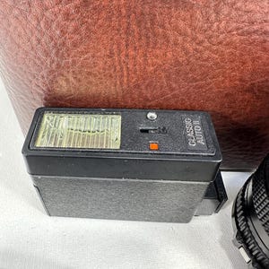 May include: A black flash unit with a clear plastic cover over the flash bulb. The flash unit has the text "CLASSIC AUTO" printed on the side.