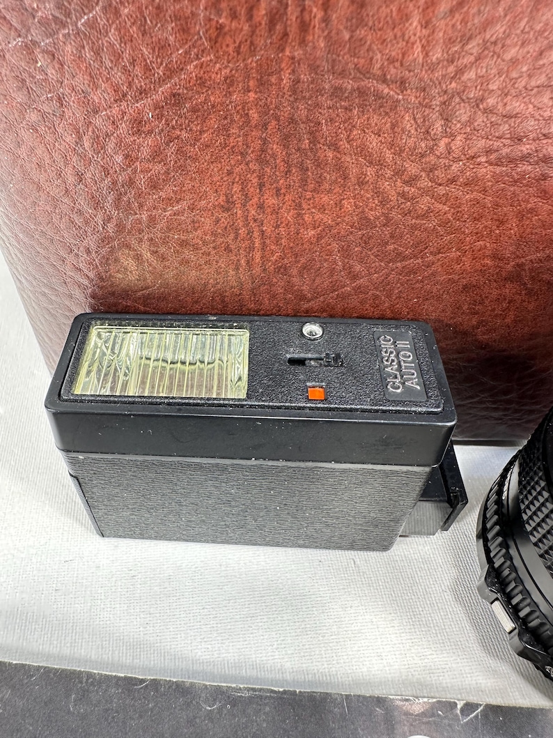 May include: A black flash unit with a clear plastic cover over the flash bulb. The flash unit has the text "CLASSIC AUTO" printed on the side.