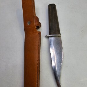 May include: A brown leather sheath with a silver rivet and a silver blade knife with a dark wood handle.