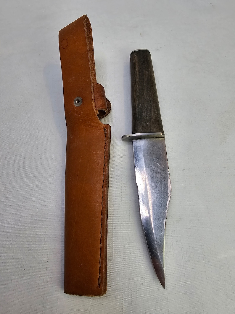 May include: A brown leather sheath with a silver rivet and a silver blade knife with a dark wood handle.