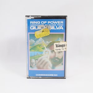 Puede incluir: Cartucho de juego de Commodore 64 para "Ring of Power" de Quicksilva. La etiqueta azul y rosa presenta un paisaje montañoso y un hombre barbudo señalando. Una etiqueta de precio amarilla está adherida.