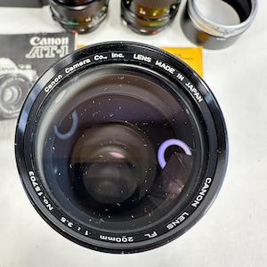 May include: A black Canon 200mm f/3.5 lens with the text "Canon Lens FL 200mm 1:3.5 No. 15703 Canon Lens Made in Japan" printed around the lens barrel.
