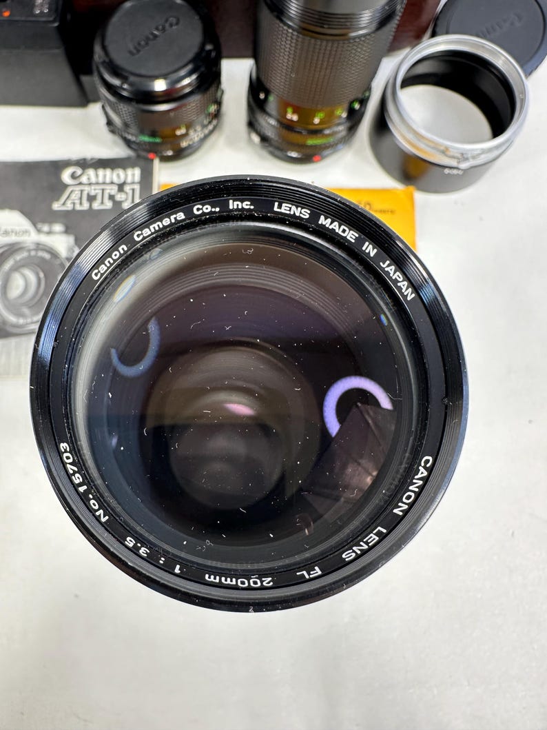May include: A black Canon 200mm f/3.5 lens with the text "Canon Lens FL 200mm 1:3.5 No. 15703 Canon Lens Made in Japan" printed around the lens barrel.