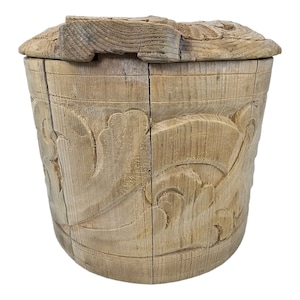 May include: A wooden box with a carved lid. The box is made of light wood and has a simple, rustic design. The lid is hinged and has a carved floral pattern.