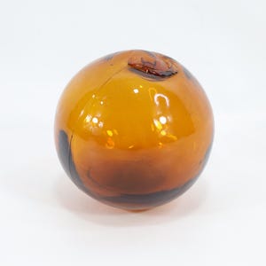 May include: A round, amber-colored glass fishing float with a small, dark brown opening at the top.