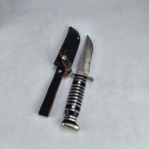 May include: A black and silver pocket knife with a black and white striped handle and a leather sheath.