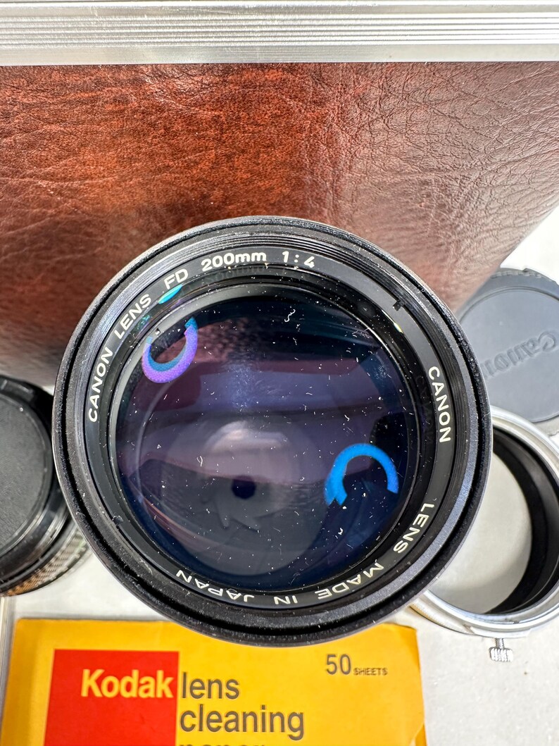 May include: A black Canon FD 200mm 1:4 lens with the text "Canon Lens FD 200mm 1:4 Canon Lens Made in Japan" printed on the side.
