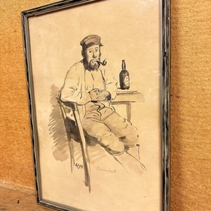 May include: A black and white drawing of a man sitting in a chair, wearing a cap and smoking a pipe. He is holding a bottle of beer in his right hand. The drawing is framed in a silver frame.