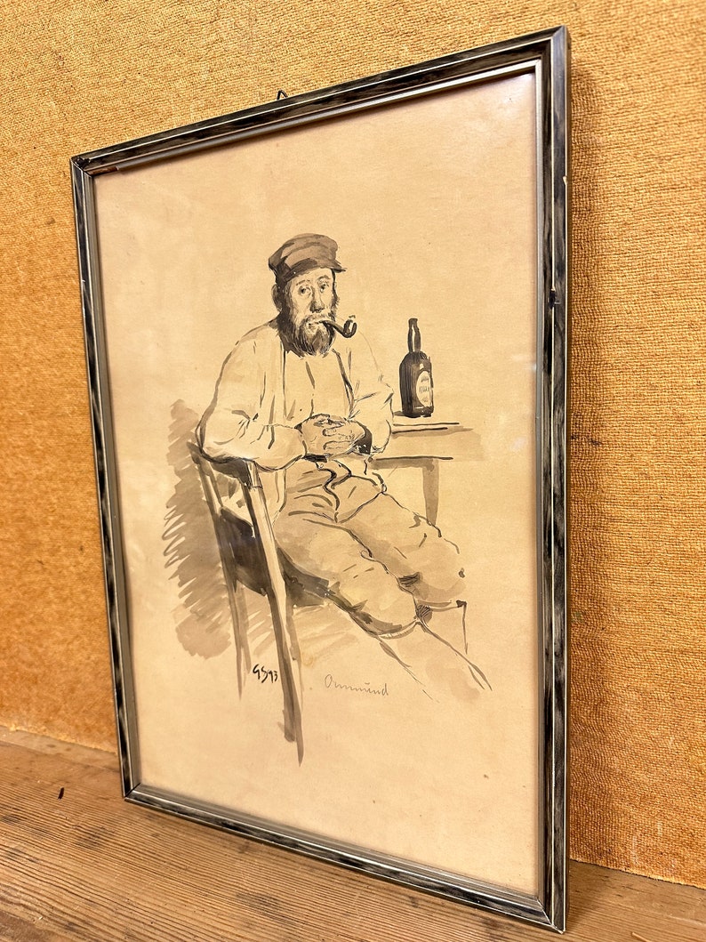 May include: A black and white drawing of a man sitting in a chair, wearing a cap and smoking a pipe. He is holding a bottle of beer in his right hand. The drawing is framed in a silver frame.