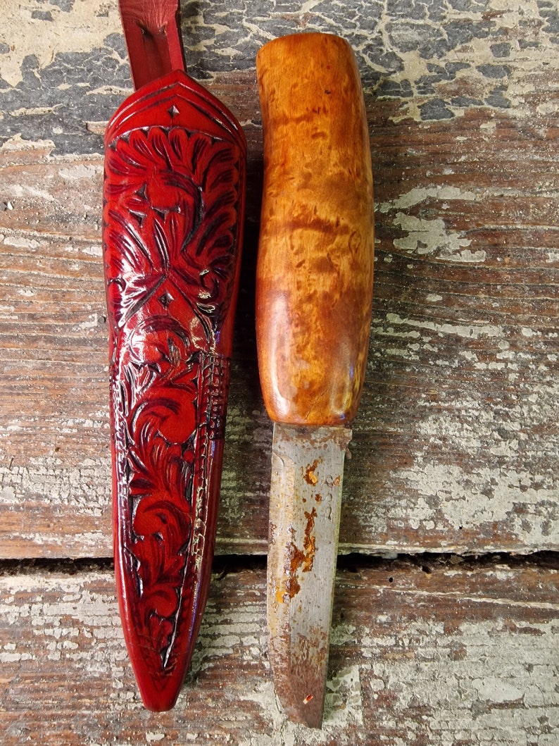 Puede incluir: Una funda de cuero roja con un intrincado dise&ntilde;o floral y un cuchillo con mango de madera y hoja de metal.