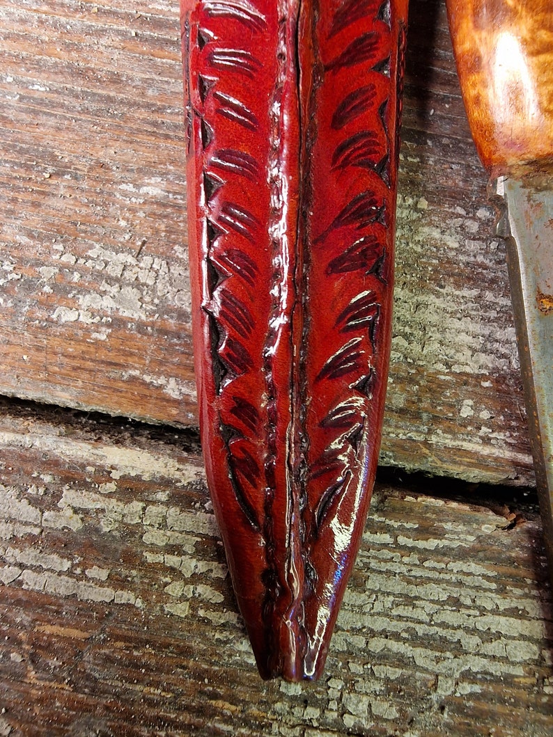 Puede incluir: Una funda de cuero roja con un patr&oacute;n decorativo de plumas. La funda est&aacute; hecha de cuero de alta calidad y tiene un acabado liso.
